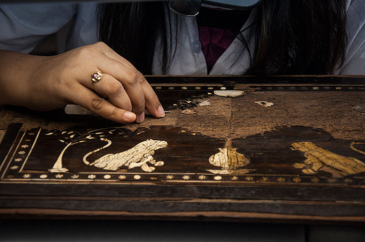 Grime and old adhesive are being cleaned from the ivory-inlaid teak wood surface of an indo-portuguese fall-front cabinet from Gujarat/Sindh (C. 17th century)